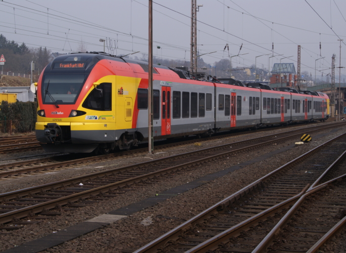 Triebwagen der Hessischen Landesbahn mit gelb-roter Front im Gleisvorfeld des Siegener Hauptbahnhofes, die Zugzielanzeige lautet "Frankfurt Hbf"
